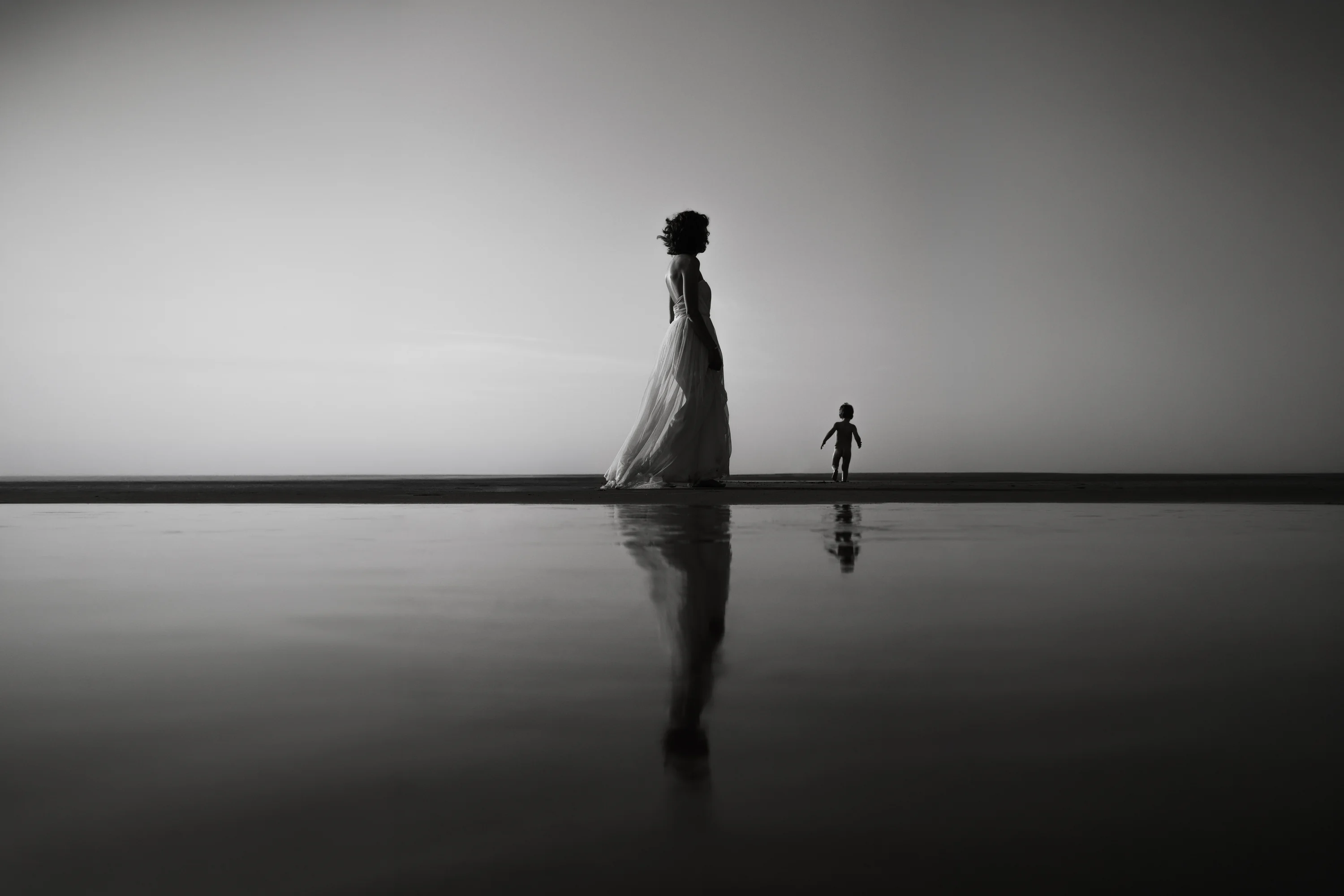 Silhouette d’une femme et d’un enfant au bord de l’eau, en noir et blanc